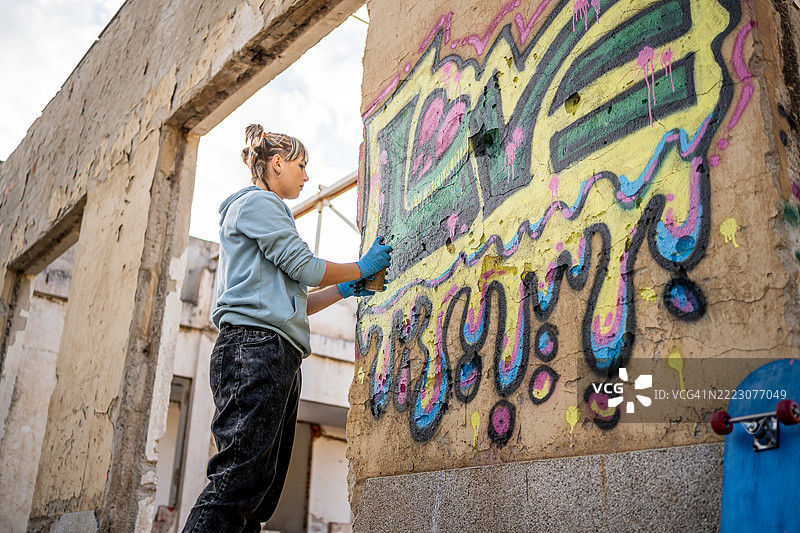 年轻艺术家在废弃建筑的墙壁上喷涂五彩斑斓的涂鸦图片素材