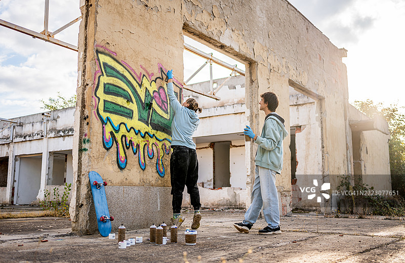 两个年轻的涂鸦艺术家在废弃建筑的墙上喷涂图片素材