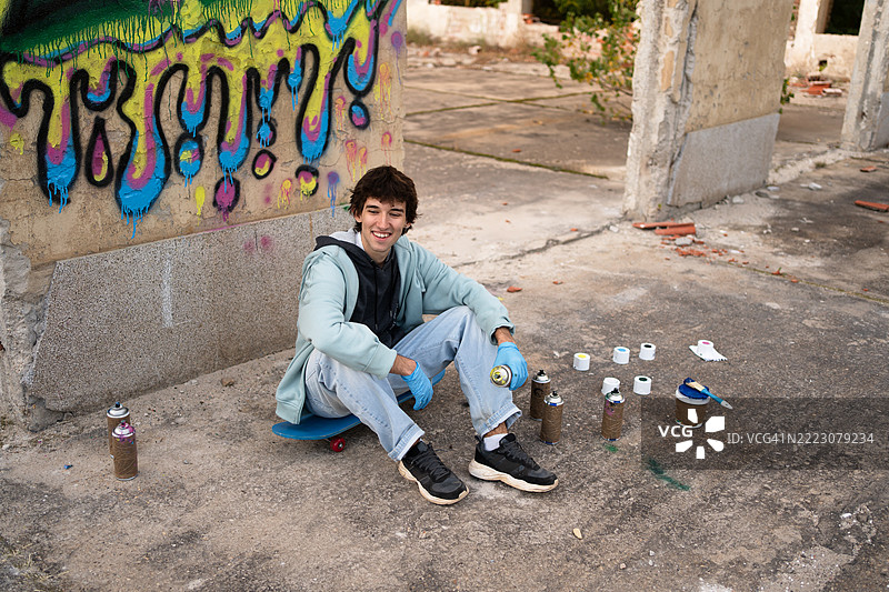 年轻男性涂鸦艺术家在废弃建筑中摆姿势，手持喷漆罐图片素材