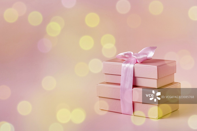 粉色背景上带有丝带的礼物粉色盒子，带有散景效果，留白空间图片素材