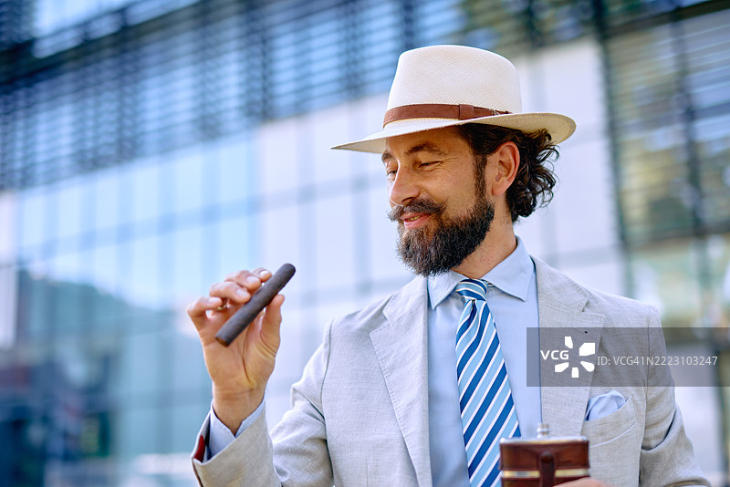 时尚的商人在现代建筑前欣赏他的雪茄图片素材