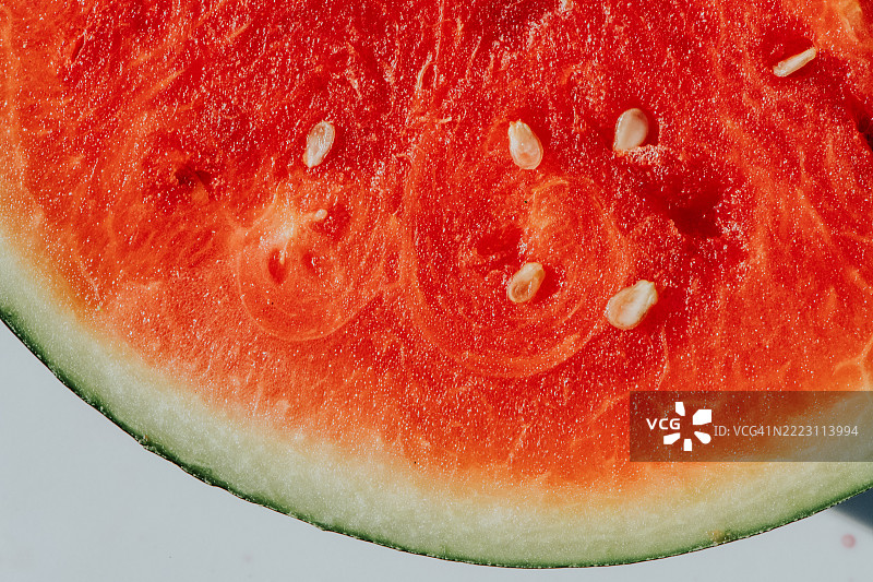 成熟西瓜的特写，鲜艳的红色果肉和散落的种子在白色背景下显得格外醒目图片素材