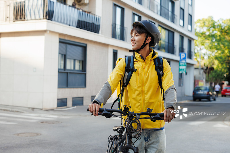 城市环境中骑自行车的快递员，背着黄色包穿过街道图片素材