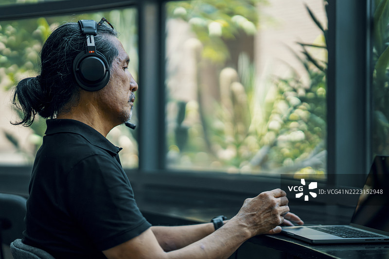 成熟男性戴着耳机和使用笔记本电脑，正在进行心理健康休息。图片素材