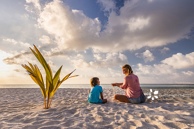 快乐的母亲和她的小男孩在海滩上谈论沙子，背影。图片素材