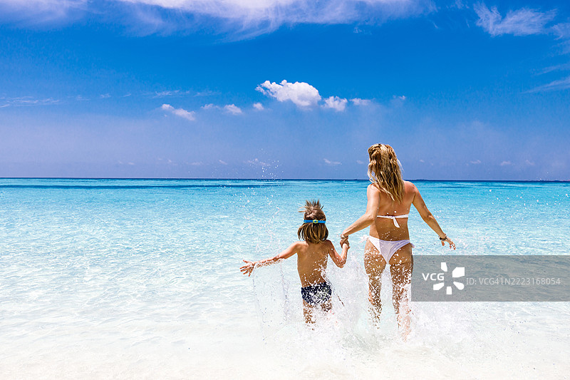 母亲和她的小儿子在海滩上奔跑的背影。图片素材