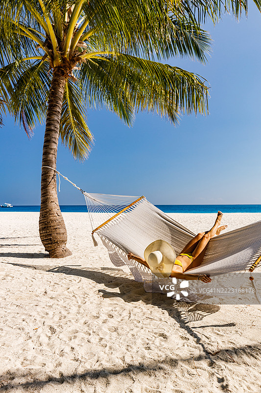 无忧无虑的女人戴着太阳帽在海滩的吊床上摇摆。图片素材