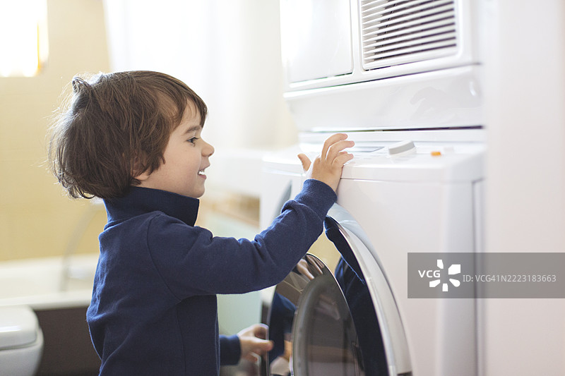 年轻孩子在明亮的家居环境中与洗衣机互动图片素材