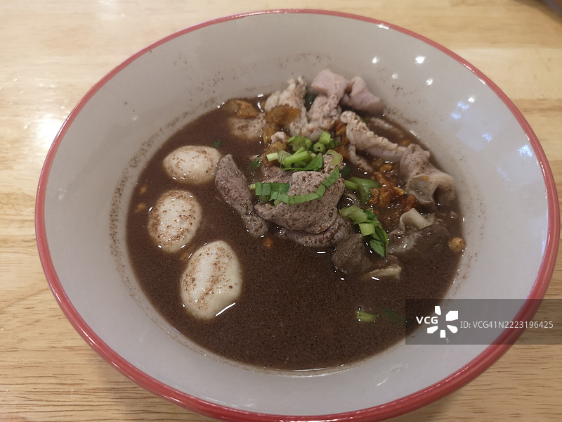 泰式面条，白碗中盛着小面条、炖猪肉、肉丸、猪肝和血汤，搭配木筷和勺子，调味后美味的泰国菜。图片素材