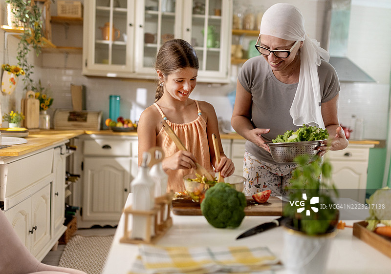 经过化疗并战胜疾病后，一位母亲在厨房与女儿一起制作健康餐。图片素材