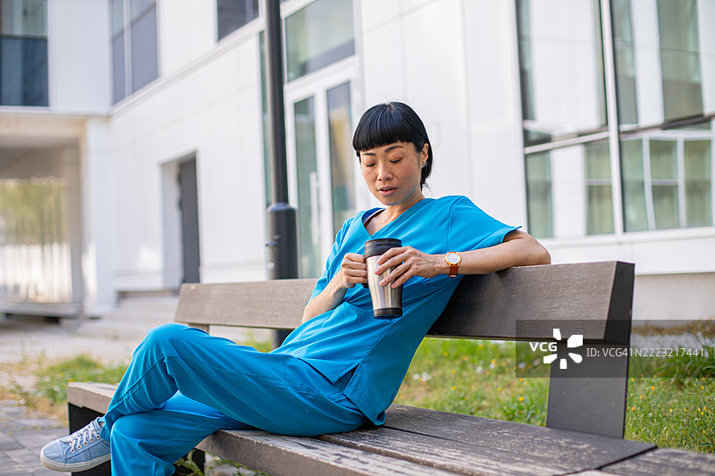疲惫的护士在户外放松，手中捧着热饮图片素材