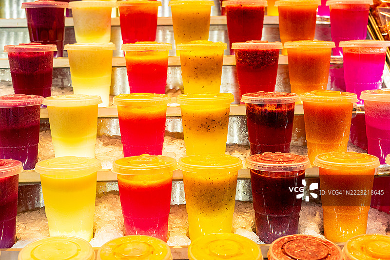 市场摊位上展示的冰上五彩缤纷的水果汁，装在塑料杯中图片素材