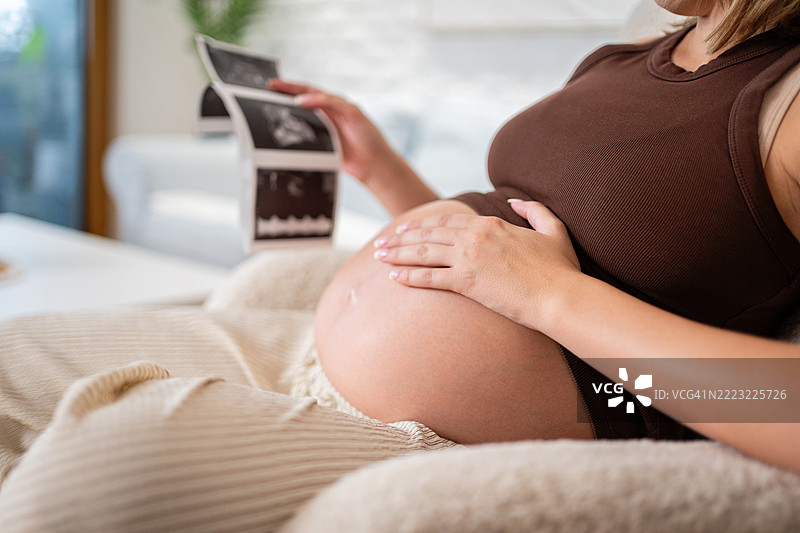 孕妈妈在舒适的家居环境中放松，手中拿着超声波图像图片素材