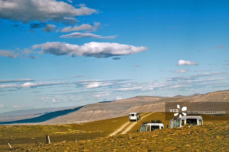 三辆旅游面包车驶离典型的巴塔哥尼亚风景。低云和蓝天。图片素材