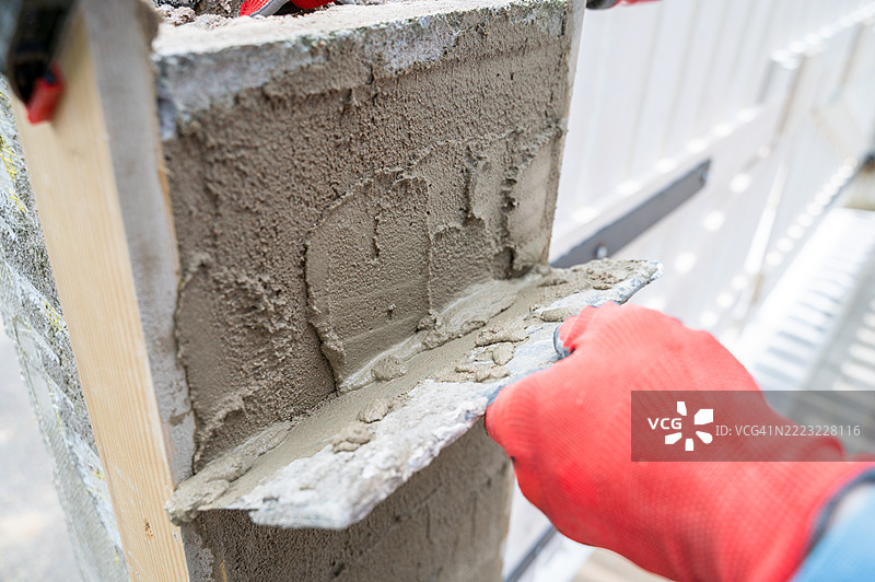 戴手套的手用抹刀在围栏柱上涂抹找平材料图片素材