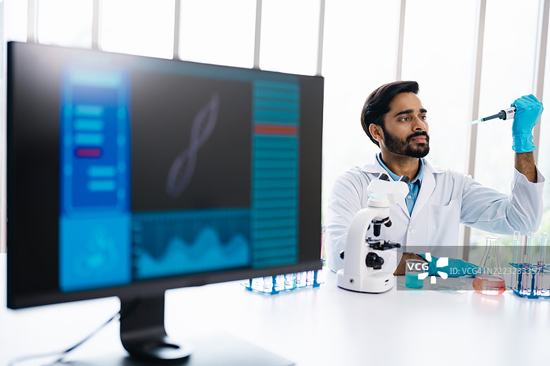 男性科学家在现代研究设施中将实验室实验与数字数据分析相结合。生物技术研究人员在进行检测的同时，分析计算机上的遗传或分子数据。图片素材