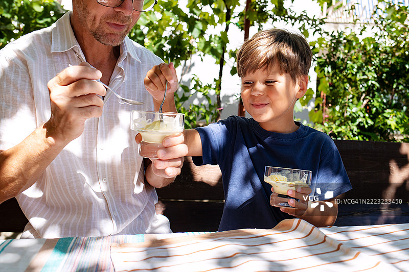 男孩在阳光明媚的露台上顽皮地从祖父手中抢走冰淇淋图片素材
