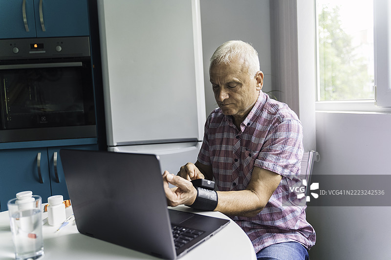老年男子在家中使用设备监测健康图片素材