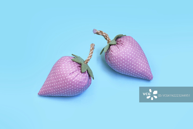 两个手工制作的粉色布草莓，背景为蓝色，作为创意DIY装饰。图片素材