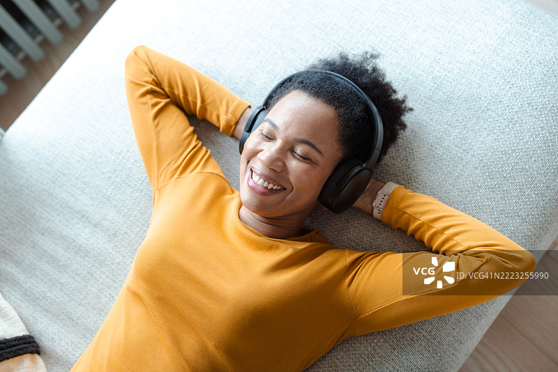 放松的成年女性戴着耳机，愉快地享受音乐并微笑。图片素材