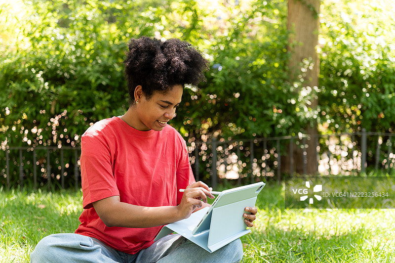 年轻学生在公园里坐着使用平板电脑图片素材