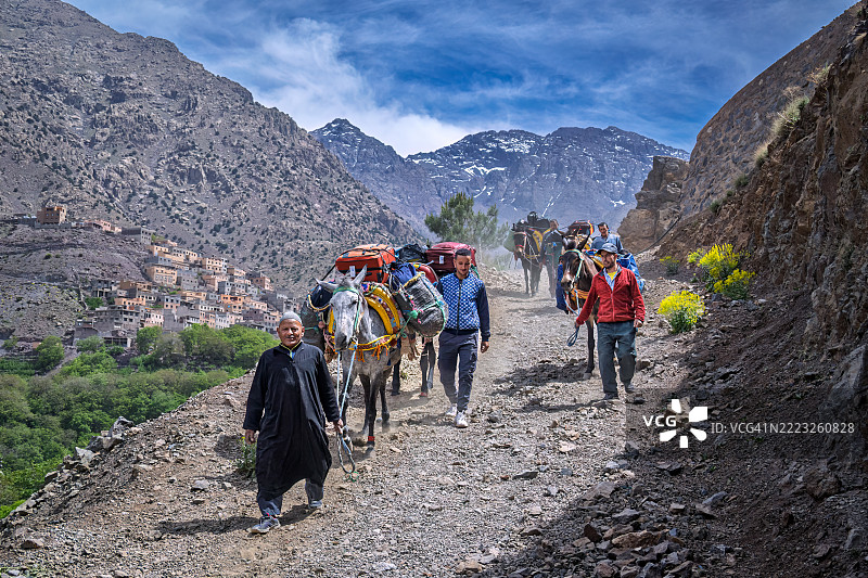 在摩洛哥伊姆利尔塔附近的土路上，驮着行李箱的骡子和搬运工。图片素材