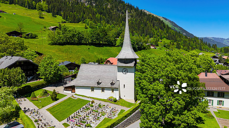 伯尔尼高地的Gsteig bei Gstaad村庄的鸟瞰图，背景是历史悠久的教堂、传统的木屋和白雪覆盖的阿尔卑斯山峰，展现瑞士乡村文化和自然旅游的概念。图片素材