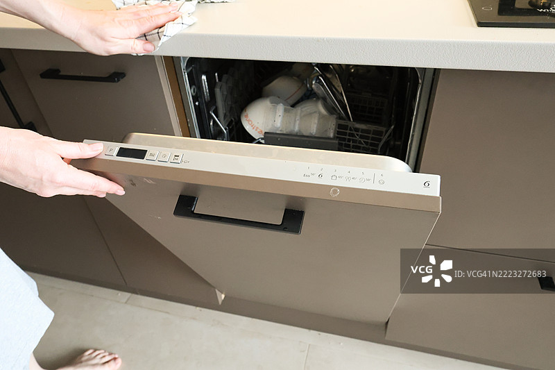 现代厨房中女性正在装载并启动洗碗机图片素材