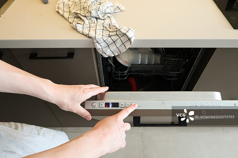 现代厨房中女性正在装载并启动洗碗机图片素材