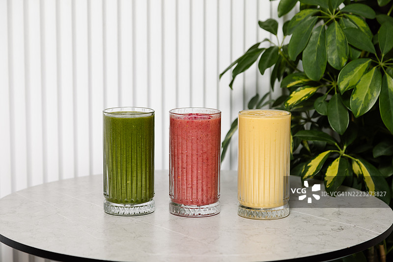 灰色桌子上的玻璃杯里装着绿色、红色和黄色的果昔图片素材