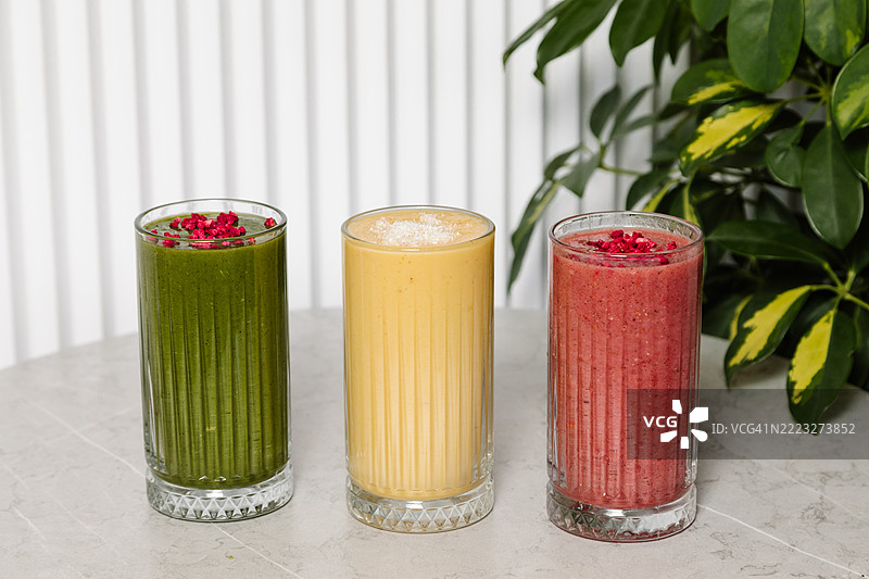 灰色桌子上的玻璃杯里装着绿色、红色和黄色的果昔图片素材
