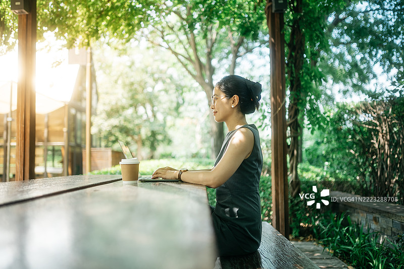 一位亚洲女商人在户外咖啡馆的树荫下使用笔记本电脑，数字游牧者图片素材