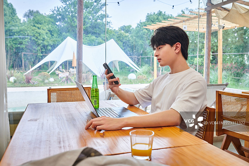 一位亚洲年轻男性在度假时喝啤酒并进行视频通话图片素材