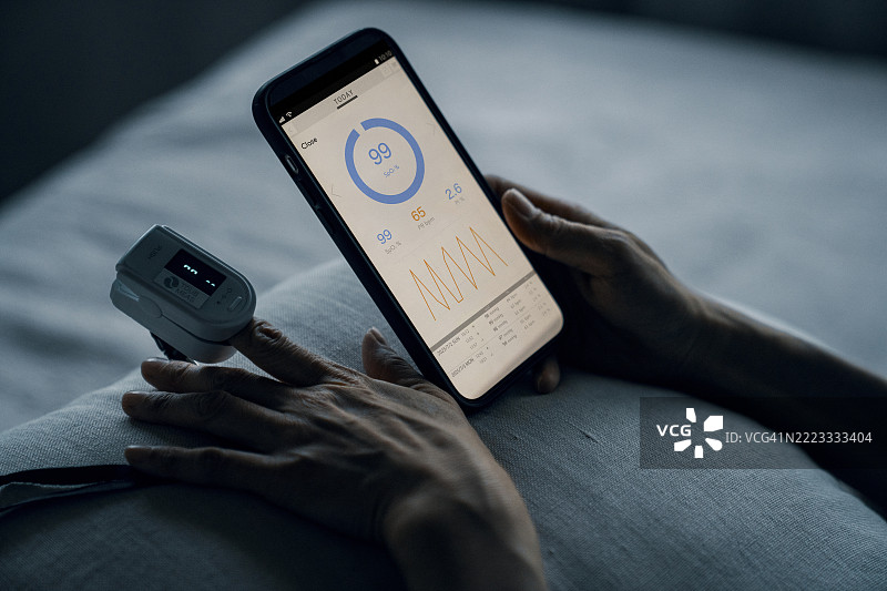成年女性从肩后视角测量氧气水平，并在智能手机上查看结果图片素材