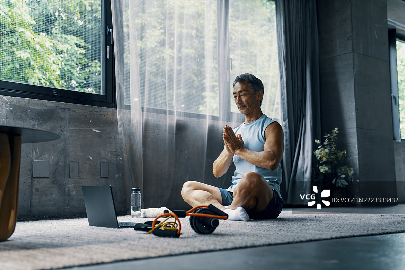一位年长男性在家锻炼，同时观看笔记本电脑。图片素材