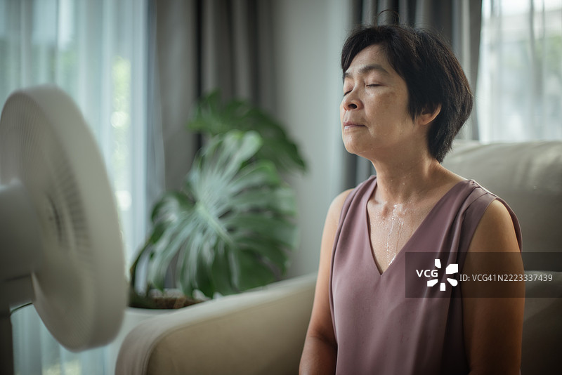 成熟的女性坐在沙发上经历潮热。图片素材