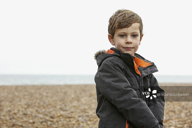 穿着夹克的可爱男孩在冬季岩石海滩上的肖像图片素材