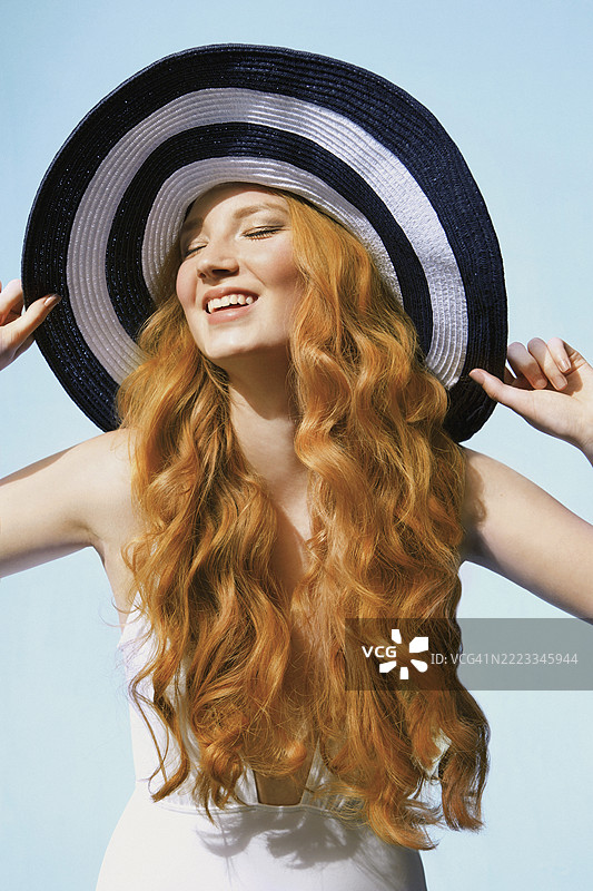 一位无忧无虑的年轻女性，长着卷曲的红发，戴着条纹帽。图片素材