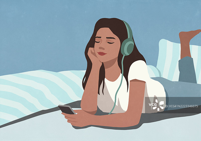 年轻女性在家中放松，躺在床上，戴着耳机听音乐，手里拿着智能手机。图片素材