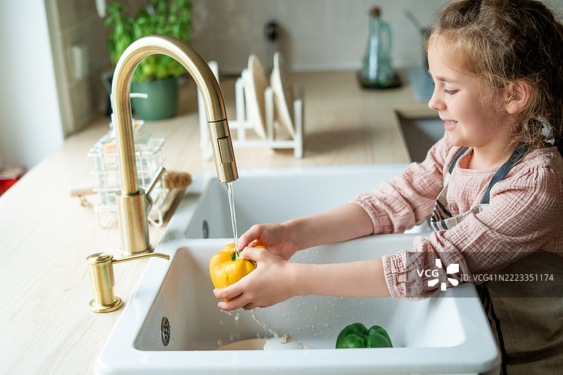 7岁的小女孩在厨房水龙头下洗蔬菜。健康饮食。图片素材