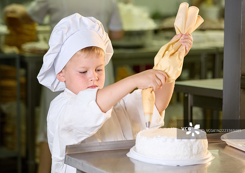可爱的男孩糕点师助手正在用奶油装饰蛋糕图片素材