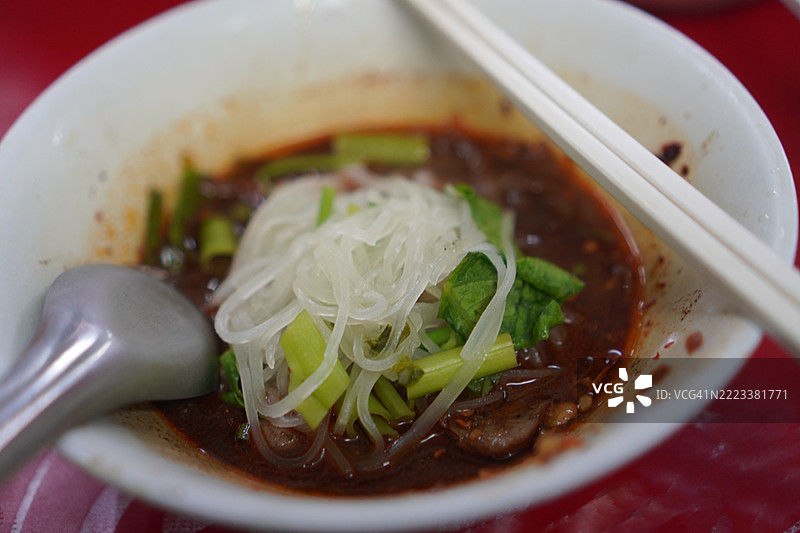 泰式面条，白碗中盛着小面条、炖猪肉、肉丸、猪肝和血汤，搭配木筷和勺子，调味后美味的泰国菜。图片素材