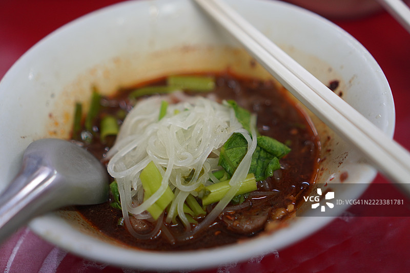泰式面条，白碗中盛着小面条、炖猪肉、肉丸、猪肝和血汤，搭配木筷和勺子，调味后美味的泰国菜。图片素材