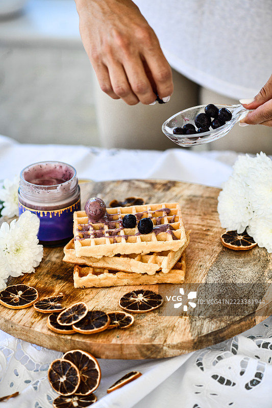 女性在木托盘上摆放覆盖果酱的华夫饼上的新鲜蓝莓图片素材