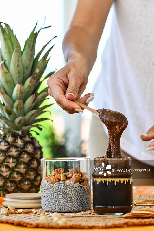 女人在准备美味的奇亚籽布丁罐，加入顺滑的巧克力酱和坚果。图片素材