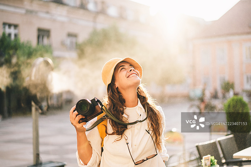 一位女性旅行者在阳光明媚的欧洲城市广场用相机拍照。图片素材