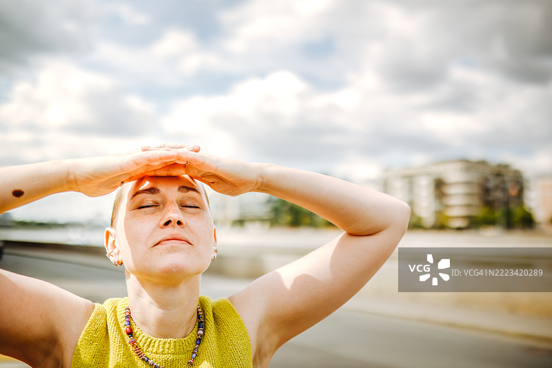 化疗后的恢复：一位头发重新生长的女性享受阳光，双手放在头后。图片素材