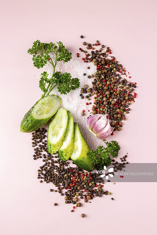 粉色背景上的黄瓜片、盐、胡椒、大蒜和香 parsley图片素材