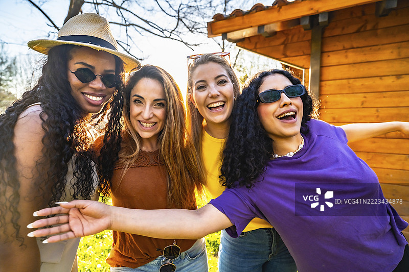 四位不同族裔的女性朋友正在花园里享受阳光明媚的一天，她们面带微笑，互相拥抱。图片素材