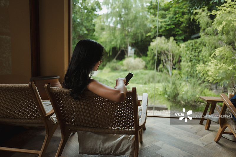 年轻女性在安静的咖啡馆里使用手机，享受宁静的氛围和绿色的景色图片素材